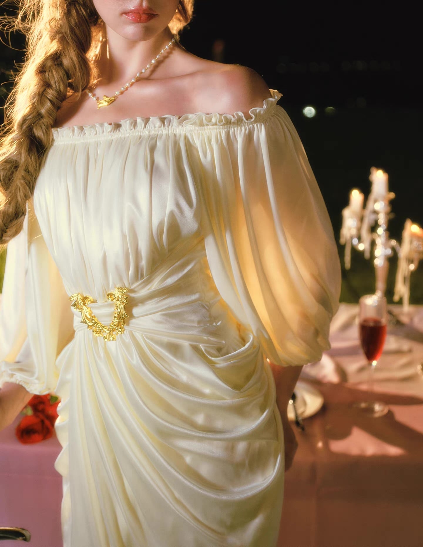 Model posing in a flowing cream satin dress with an off-the-shoulder neckline and lantern sleeves.
