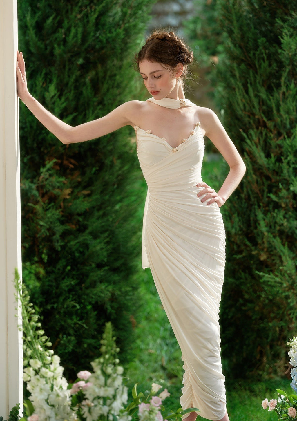 Full body shot of a woman wearing a cream-colored silk satin mermaid gown with a draped effect and scarf neckline.