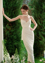 Full body shot of a woman wearing a cream-colored silk satin mermaid gown with a draped effect and scarf neckline.