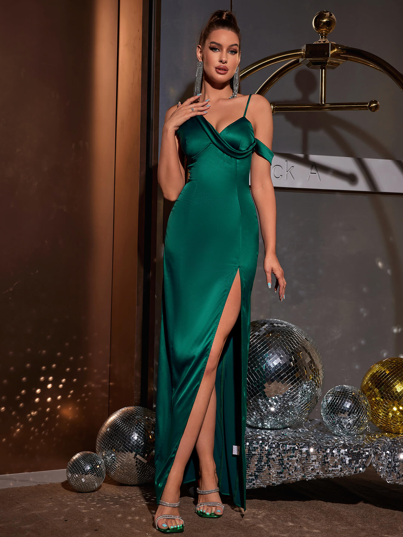 Woman posing in a green satin one-shoulder evening gown with a high slit and draped bodice.