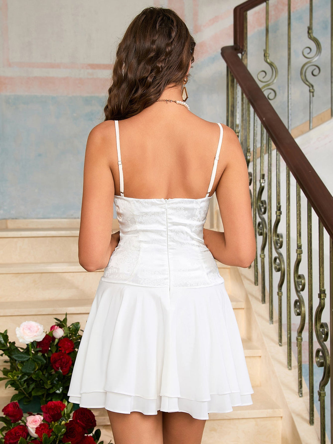 Woman wearing a white satin dress with lace overlay and a pleated skirt, standing on stairs.
