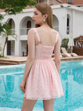 Back view of a woman in a pink textured floral mini dress with a smocked back panel and adjustable straps.