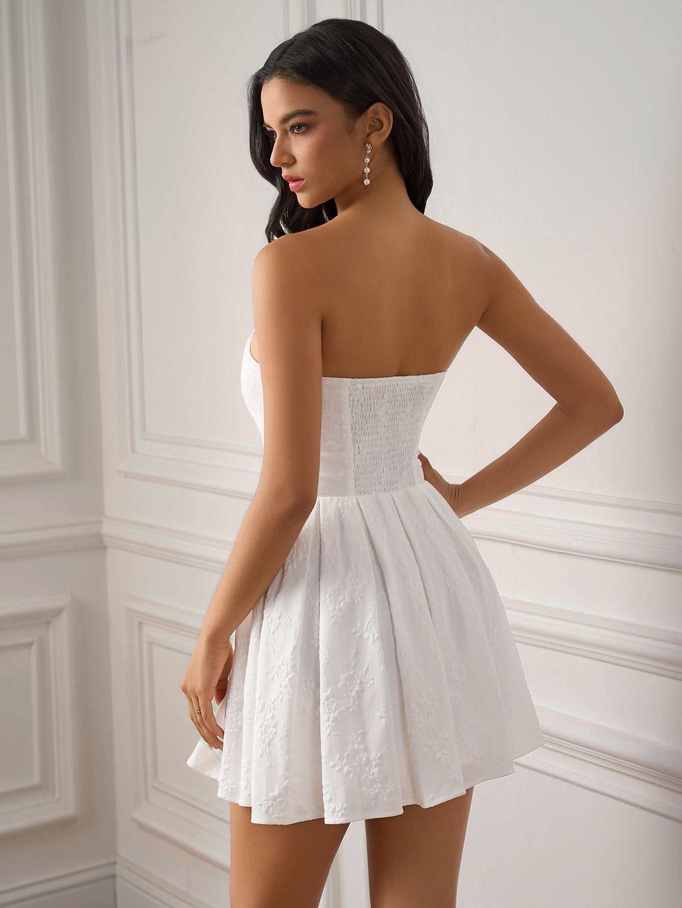 Rear view of a woman in a white strapless embroidered dress with a smocked back and a pleated skirt.