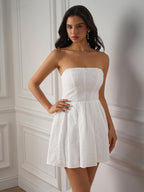 Woman wearing a white strapless embroidered dress with a pleated skirt, standing with her hand on her hip.