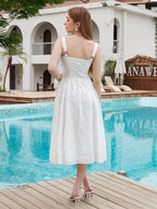 Back view of a woman in a white eyelet embroidered midi dress with a lace-up back detail, standing by a pool.