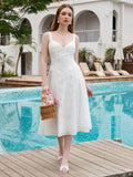 Woman holding a small woven basket with flowers, wearing a white eyelet embroidered midi dress, standing by a pool.