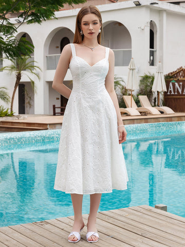 Woman wearing a white eyelet embroidered midi dress with V-neck and adjustable straps, standing on a wooden deck by a pool.