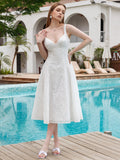 Woman in a white eyelet embroidered midi dress with a V-neck and adjustable straps, hands on her hip, standing by a pool.