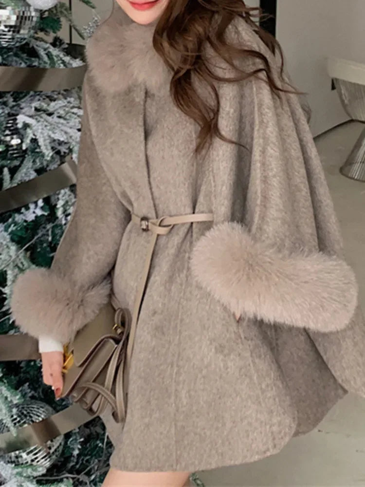 Woman wearing a beige wool blend cape with fur trim collar and cuffs, with a belt.