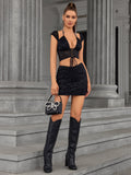 Full body shot of a woman in a black lace two-piece set, holding a small black purse and wearing tall black boots.