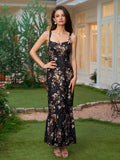 Woman in a black floral print maxi dress with a square neckline and ruffled fishtail hem, standing in a garden.