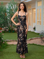 Woman in a black floral print maxi dress with a square neckline and ruffled fishtail hem, standing in a garden.