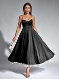 Full length shot of a woman in a black satin fit and flare midi dress holding a silver handbag.