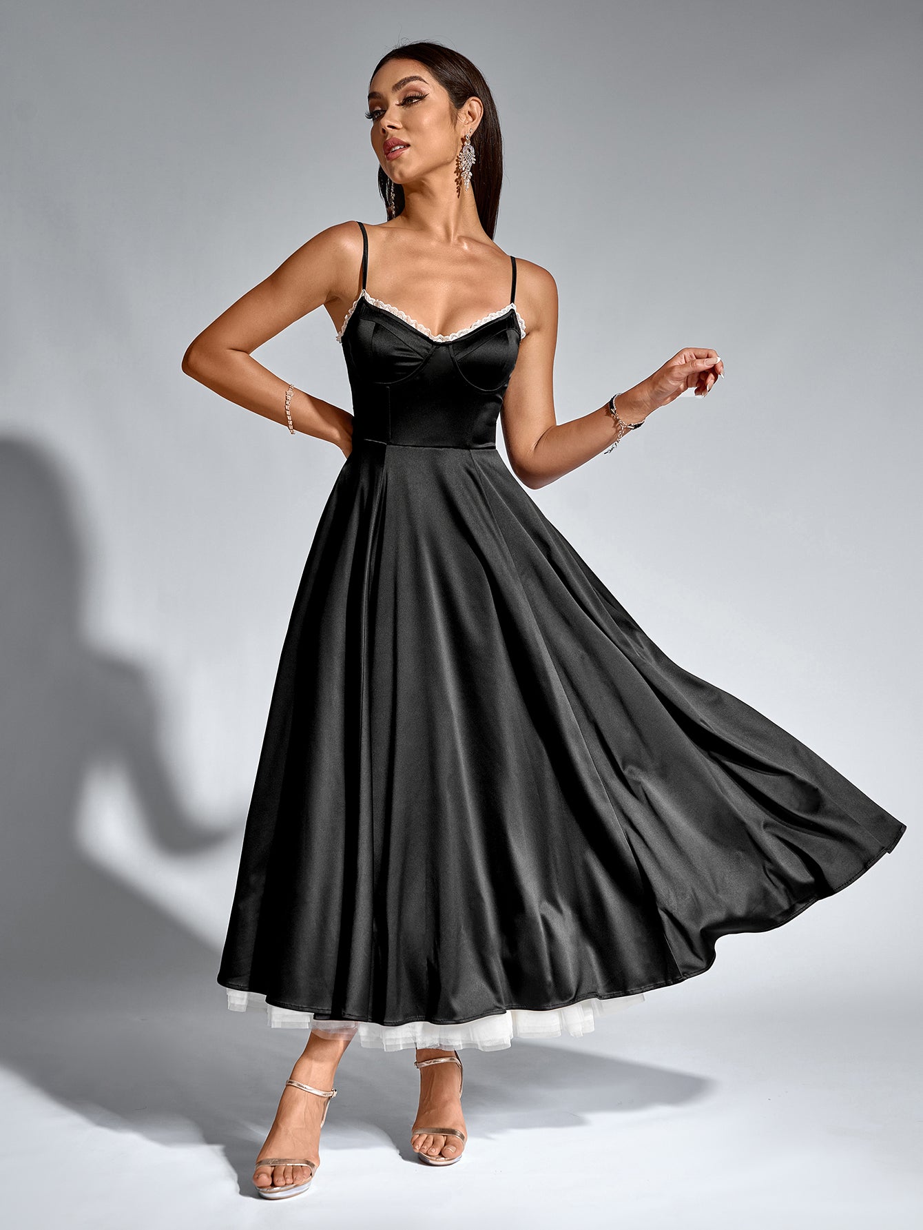 Woman in a black satin fit and flare midi dress with spaghetti straps and lace trim.