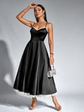 Woman posing in a black satin fit and flare midi dress with a small silver handbag.