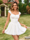 Woman wearing a white fit-and-flare mini dress with lace trim and a square neckline in a garden setting.