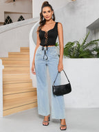 Full body shot of a woman wearing a black lace-trimmed lace-up crop top, light wash wide-leg jeans, and carrying a black handbag