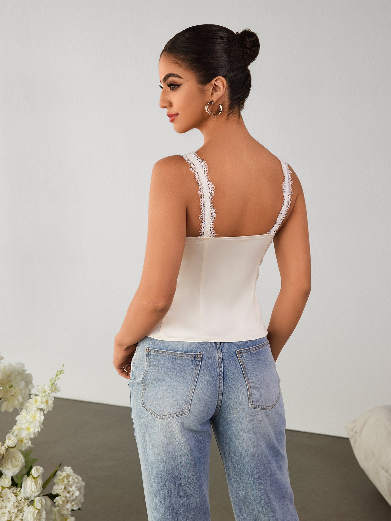 Back view of a woman in a white satin camisole with lace trim.