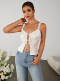 Woman posing in a white satin camisole with lace trim and tie-front detail, and light-wash denim jeans.