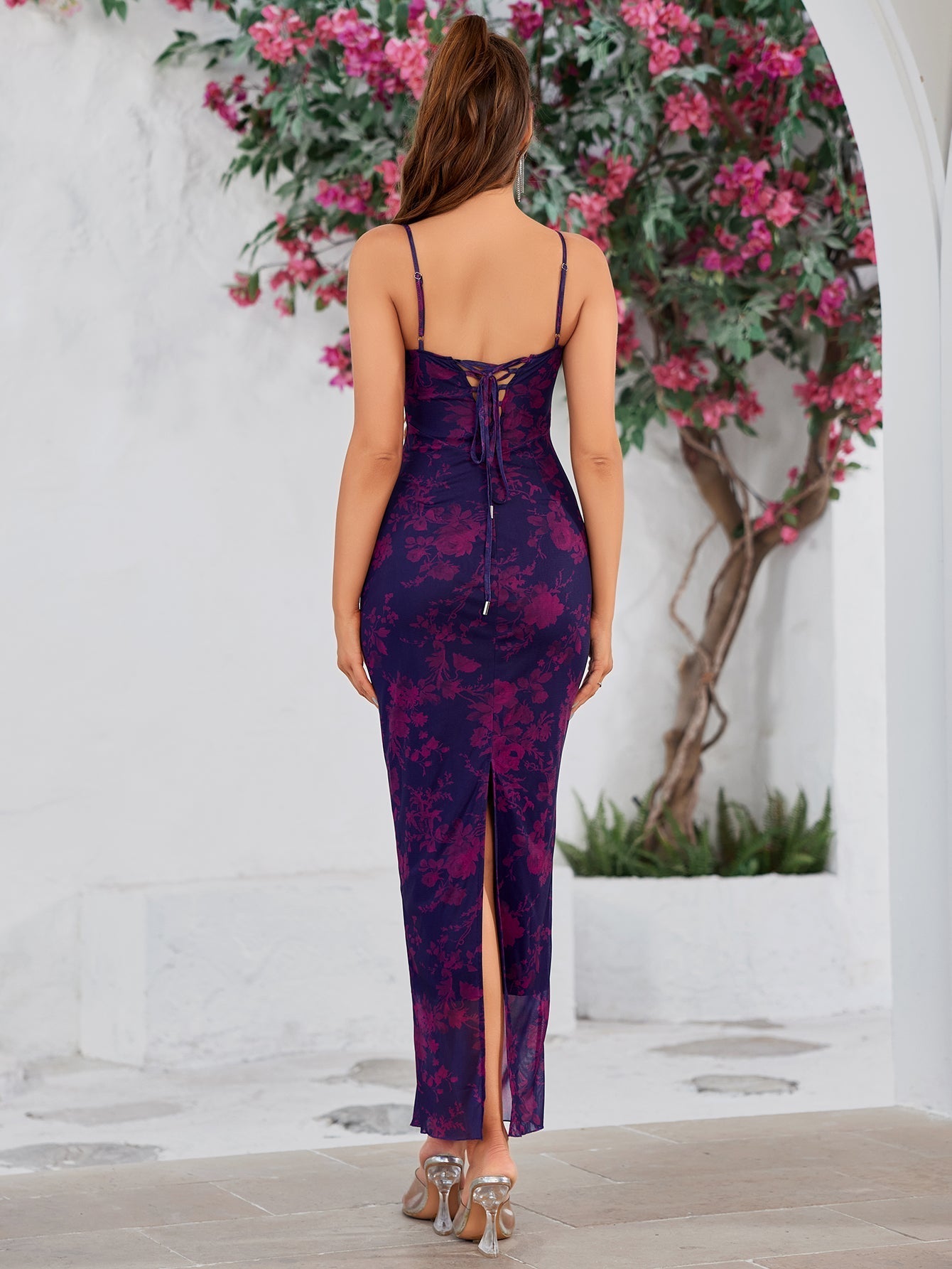 Back view of a woman in a purple and pink floral print maxi dress with a lace-up back detail and a side slit.