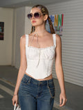Woman with sunglasses wearing a white cropped corset top with lace trim and bow detail.