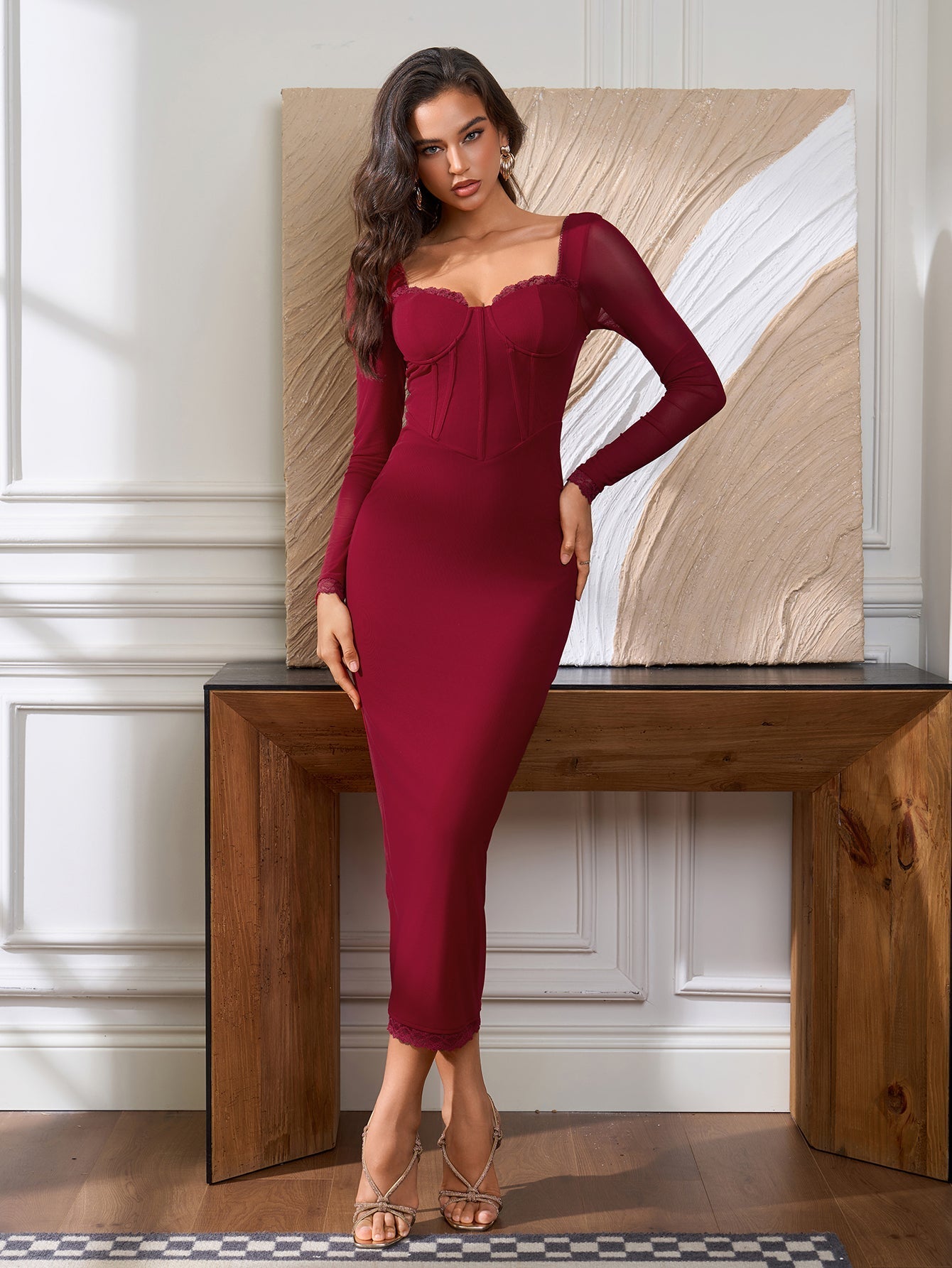 Woman posing in a fitted red dress with long sleeves and lace trim in a room with artwork.