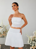 Woman posing in a white strapless cropped top with a tie front and eyelet detail, and a white tiered mini skirt with a smocked waistband.