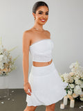 Full body shot of a smiling woman in a white strapless cropped top and a white tiered mini skirt with a smocked waistband.