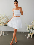 Woman in a white strapless cropped top and a white tiered mini skirt with a smocked waistband, showcasing the outfit from the front.