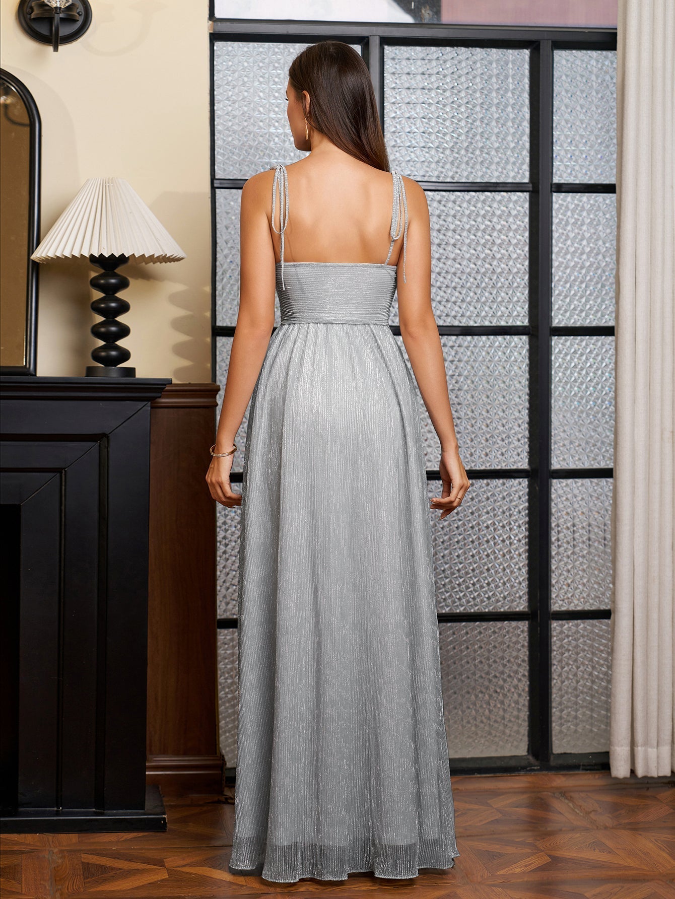 Back view of a woman in a silver metallic lurex A-line evening gown with a sweetheart neckline and cut-out waist.