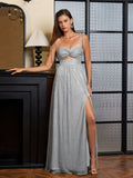 Woman in a silver metallic lurex A-line evening gown with a sweetheart neckline and cut-out waist, posing by a fireplace.