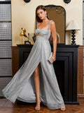 Woman in a silver metallic lurex A-line evening gown with a sweetheart neckline, cut-out waist, and high slit, holding a clutch, posing by a fireplace.