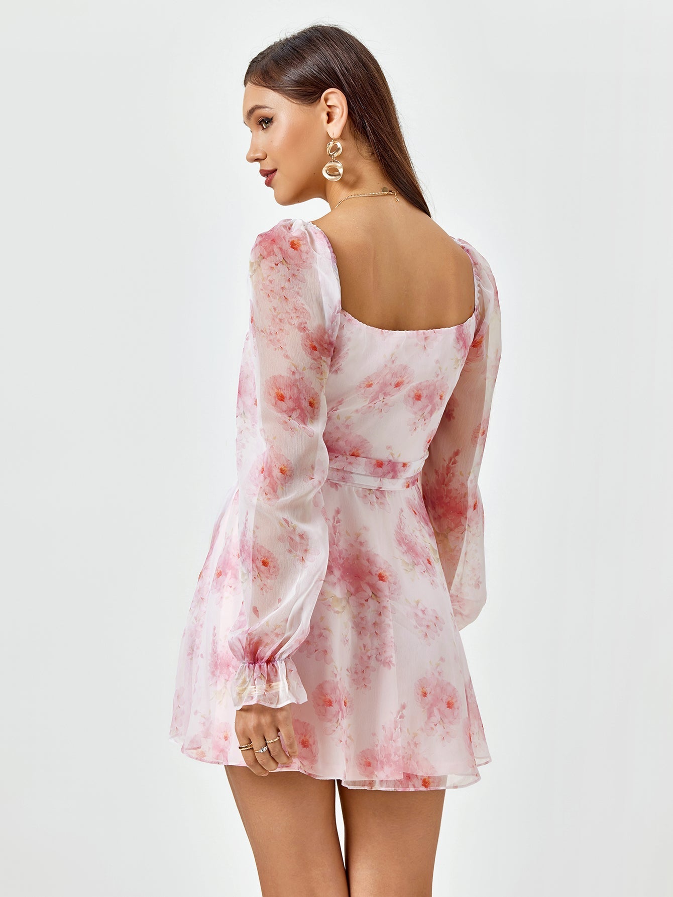 Back view of a woman in a pink floral print chiffon dress with long sleeves.