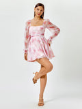 Full-body shot of a woman posing in a pink floral print chiffon dress with long sleeves.