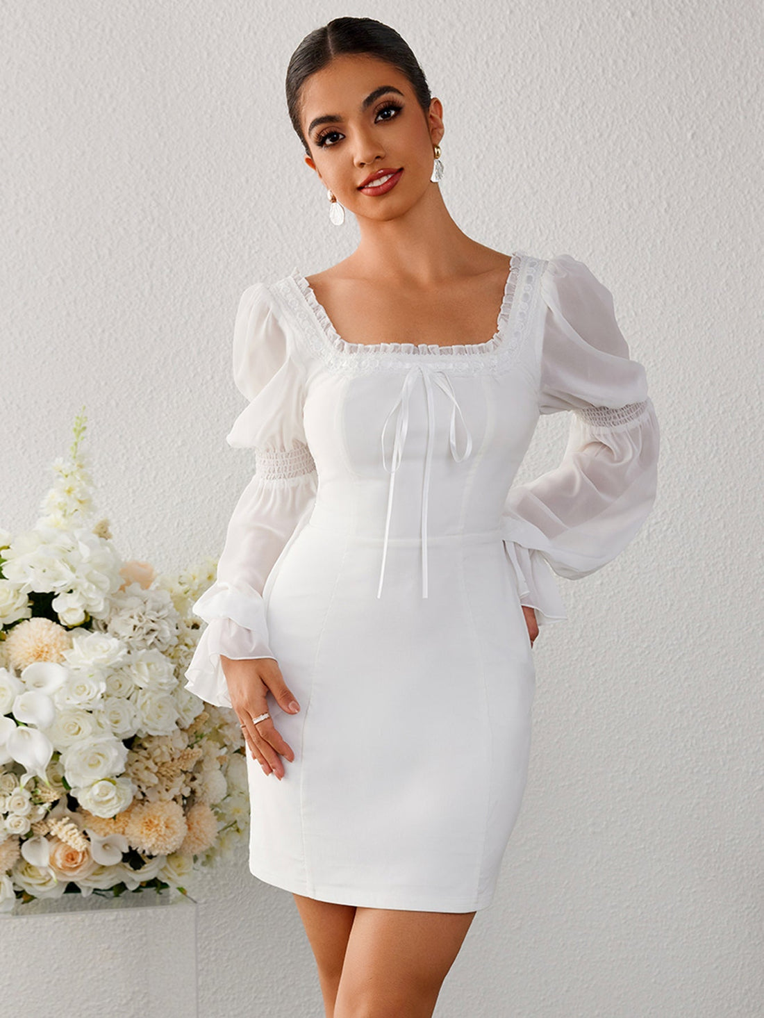 Woman in a white sheath dress with sheer bishop sleeves and a square neckline.
