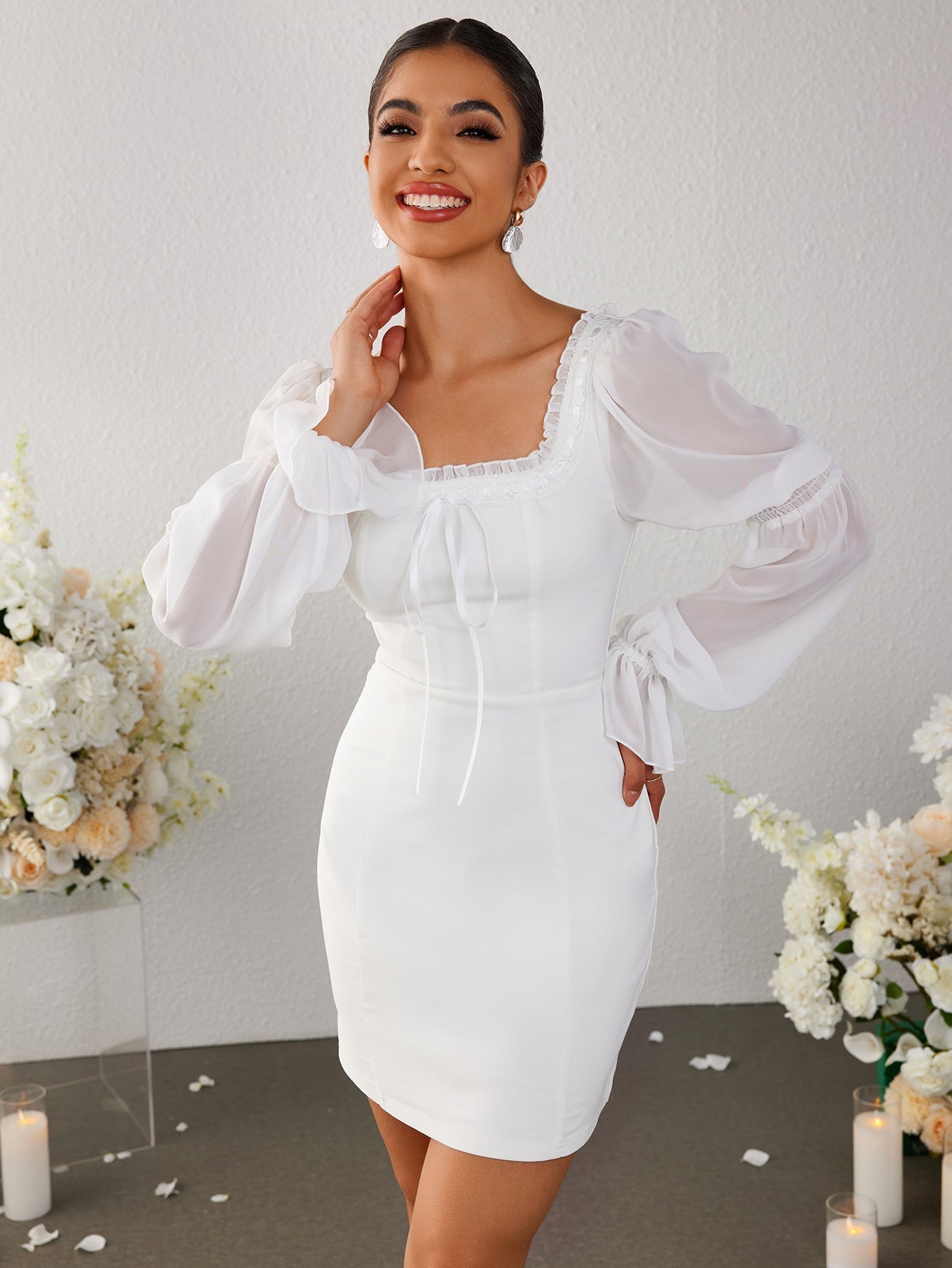 Woman posing in a white sheath dress with sheer bishop sleeves.