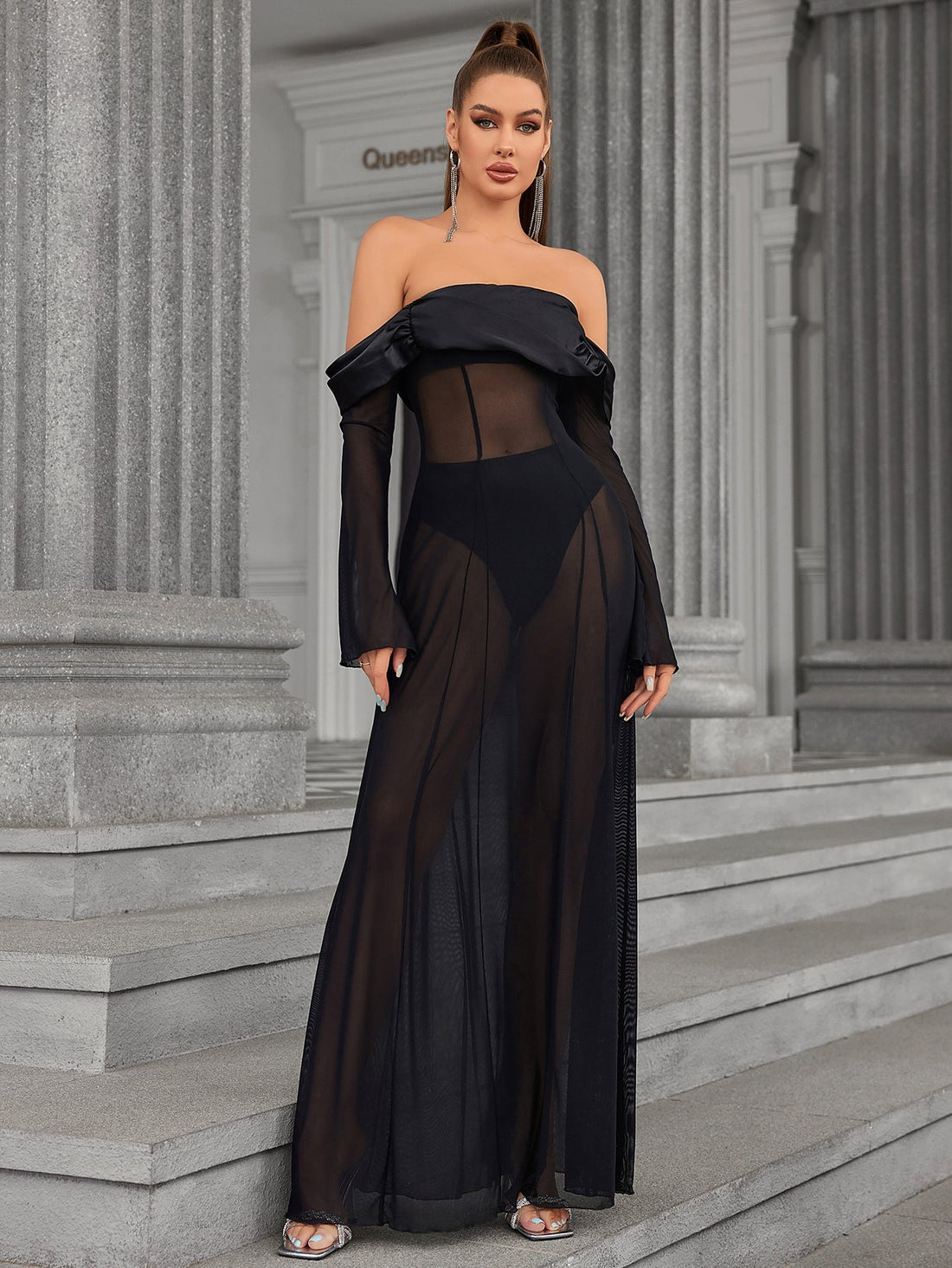 Woman wearing a black off-the-shoulder sheer mesh maxi dress with long flared sleeves.