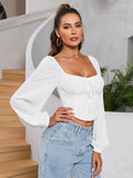 Front view of a woman posing in a white long sleeve cropped top and blue jeans.
