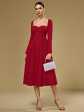 Woman holding a silver clutch while wearing a red crepe fit and flare midi dress with a sweetheart neckline and long sleeves.