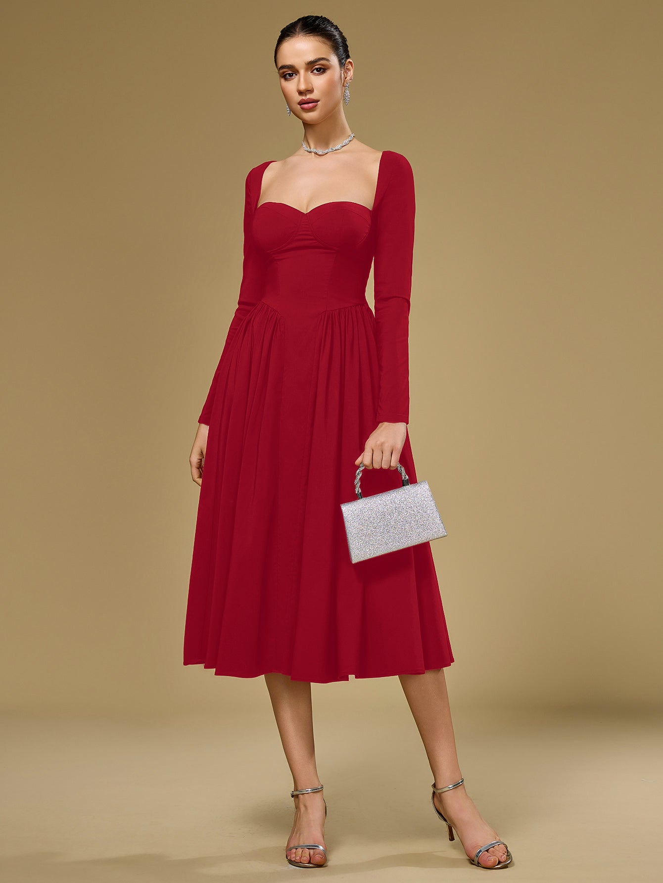 Woman holding a silver clutch while wearing a red crepe fit and flare midi dress with a sweetheart neckline and long sleeves.