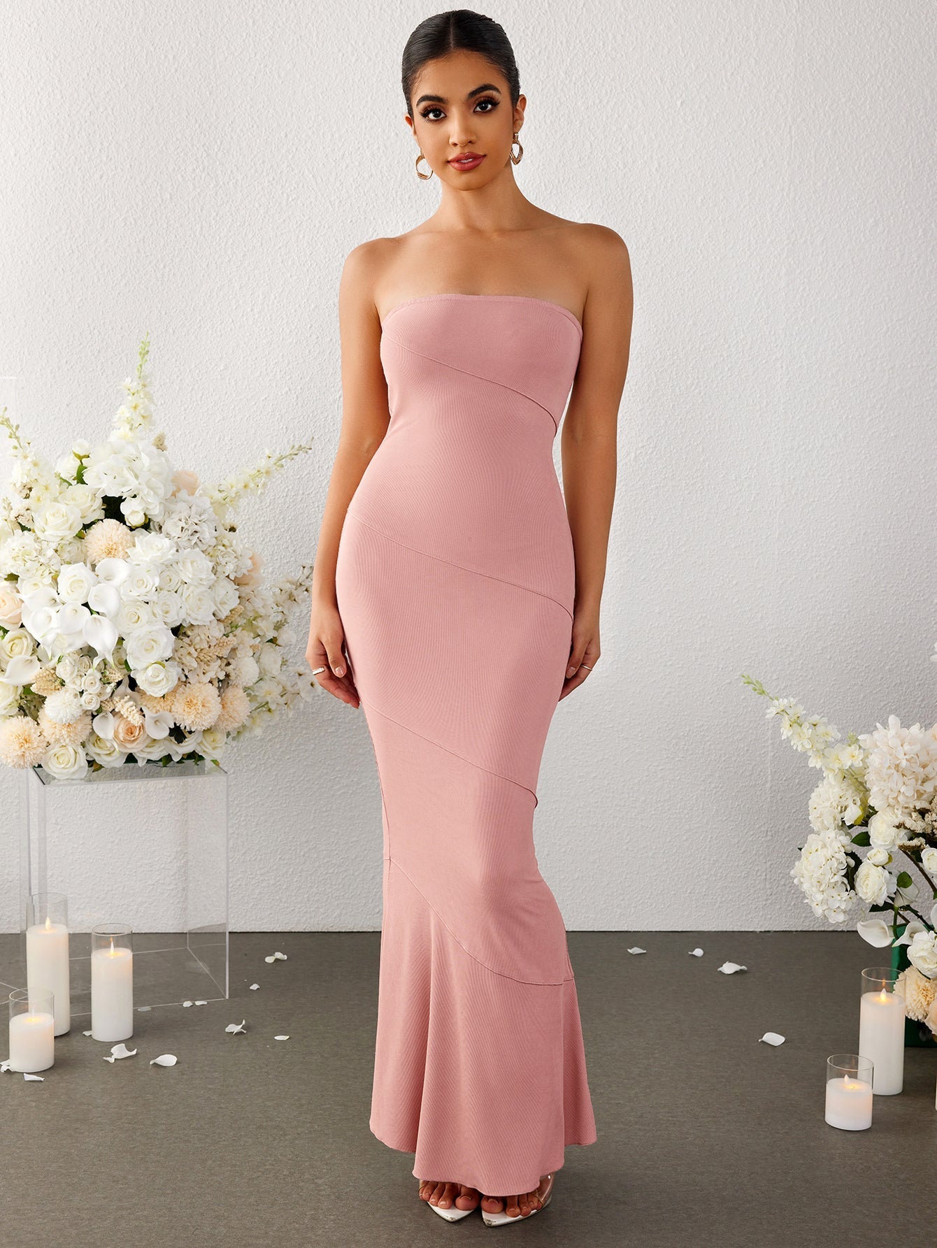 Model posing in a pink strapless ribbed knit mermaid maxi dress with floral arrangements
