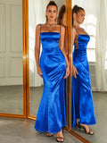 Front view of a woman in a royal blue satin mermaid evening gown, accessorized with statement jewelry and a clutch.