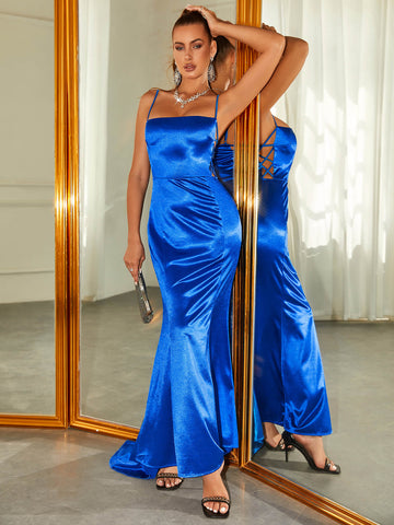Woman wearing a royal blue satin mermaid evening gown with spaghetti straps and a square neckline, posing by a mirror.