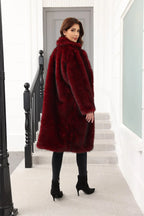 Rear view of a woman wearing a long, dark red faux fur coat with a relaxed fit, standing on stairs.