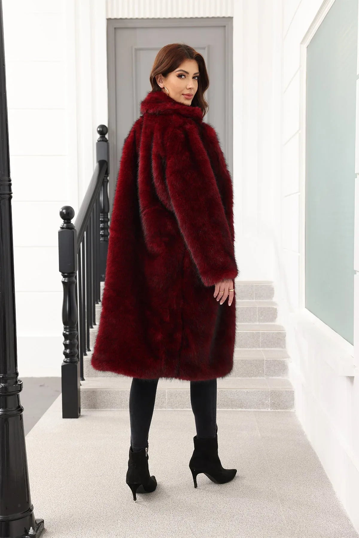 Rear view of a woman wearing a long, dark red faux fur coat with a relaxed fit, standing on stairs.