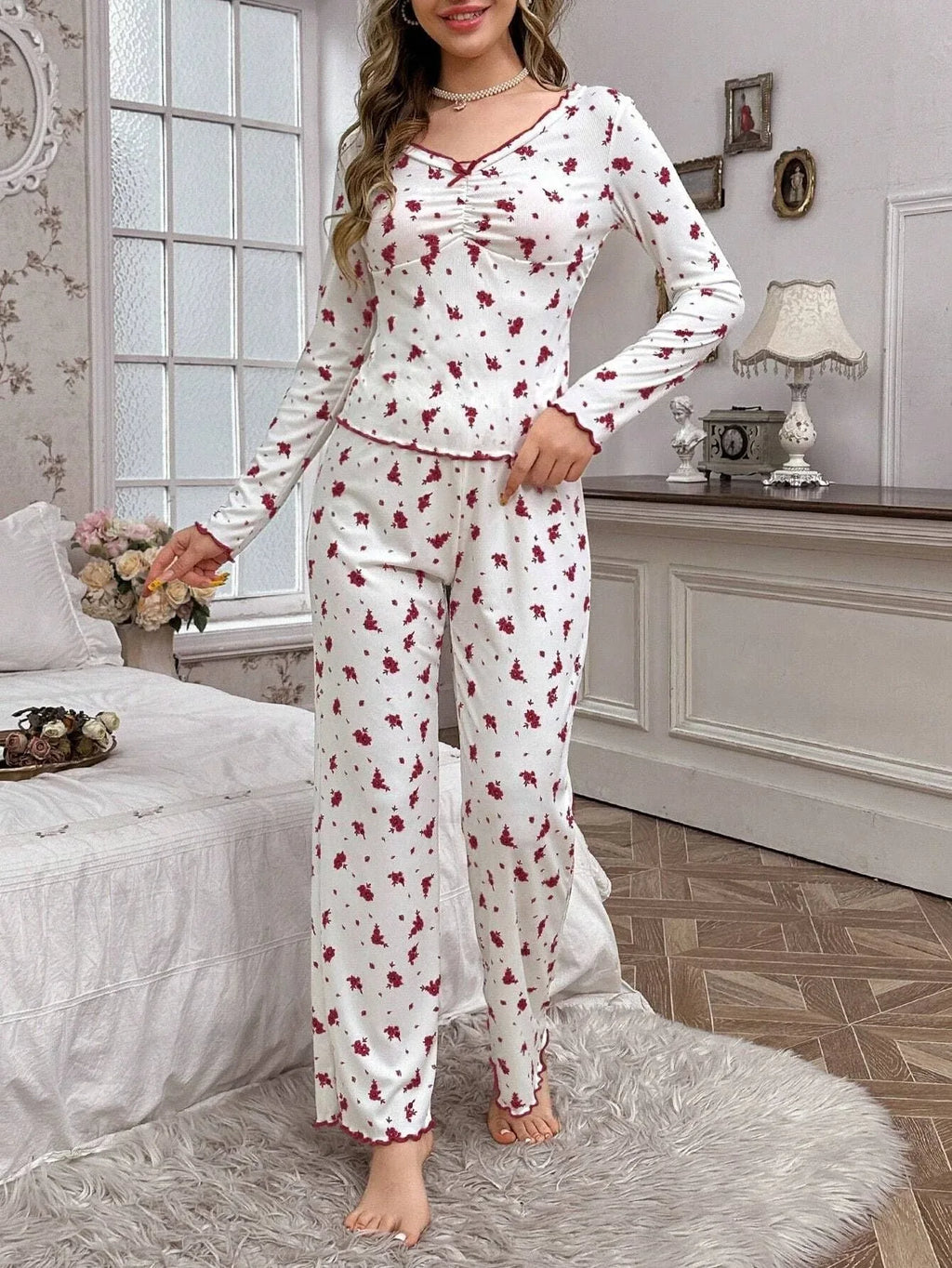 Woman wearing white long-sleeved pajamas with a red floral print and scalloped trim.