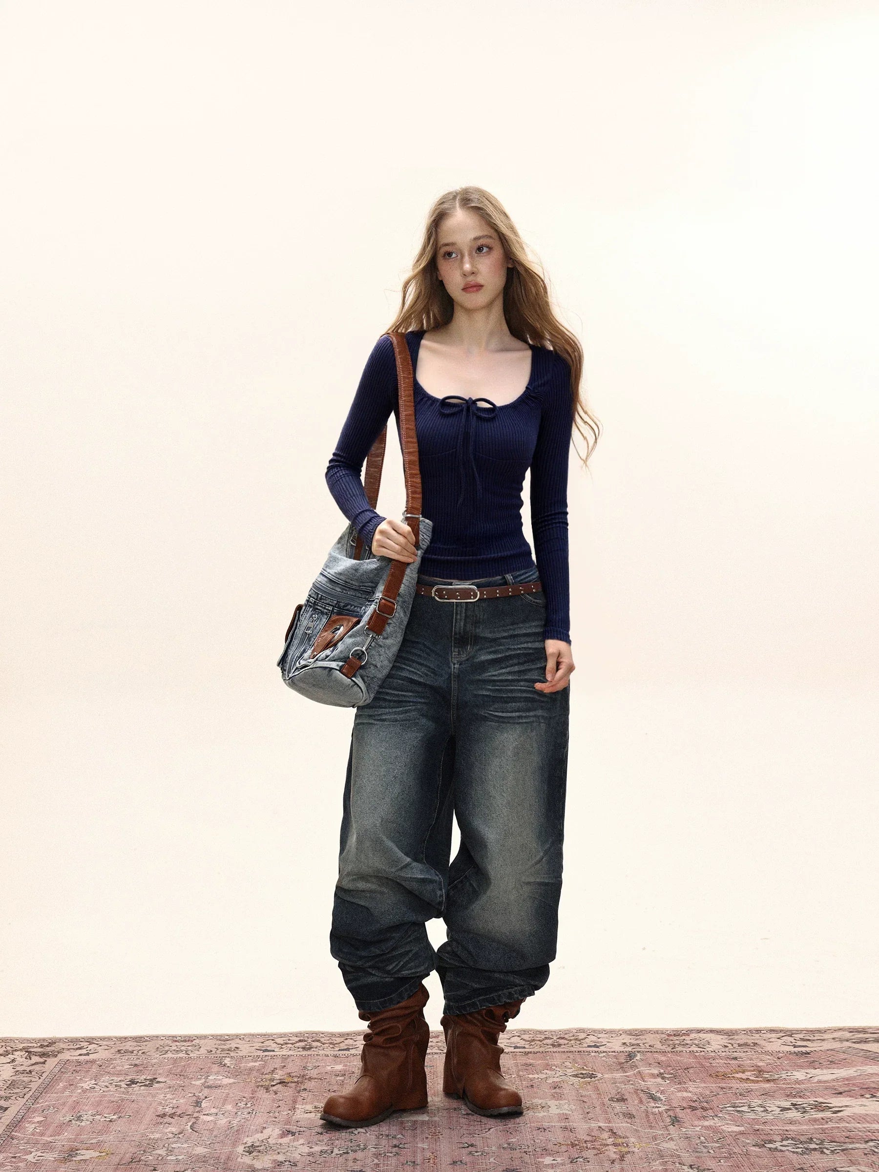 Woman wearing a navy long-sleeve ribbed knit top with a tie-front detail and scoop neckline, paired with wide-leg jeans and a crossbody bag.
