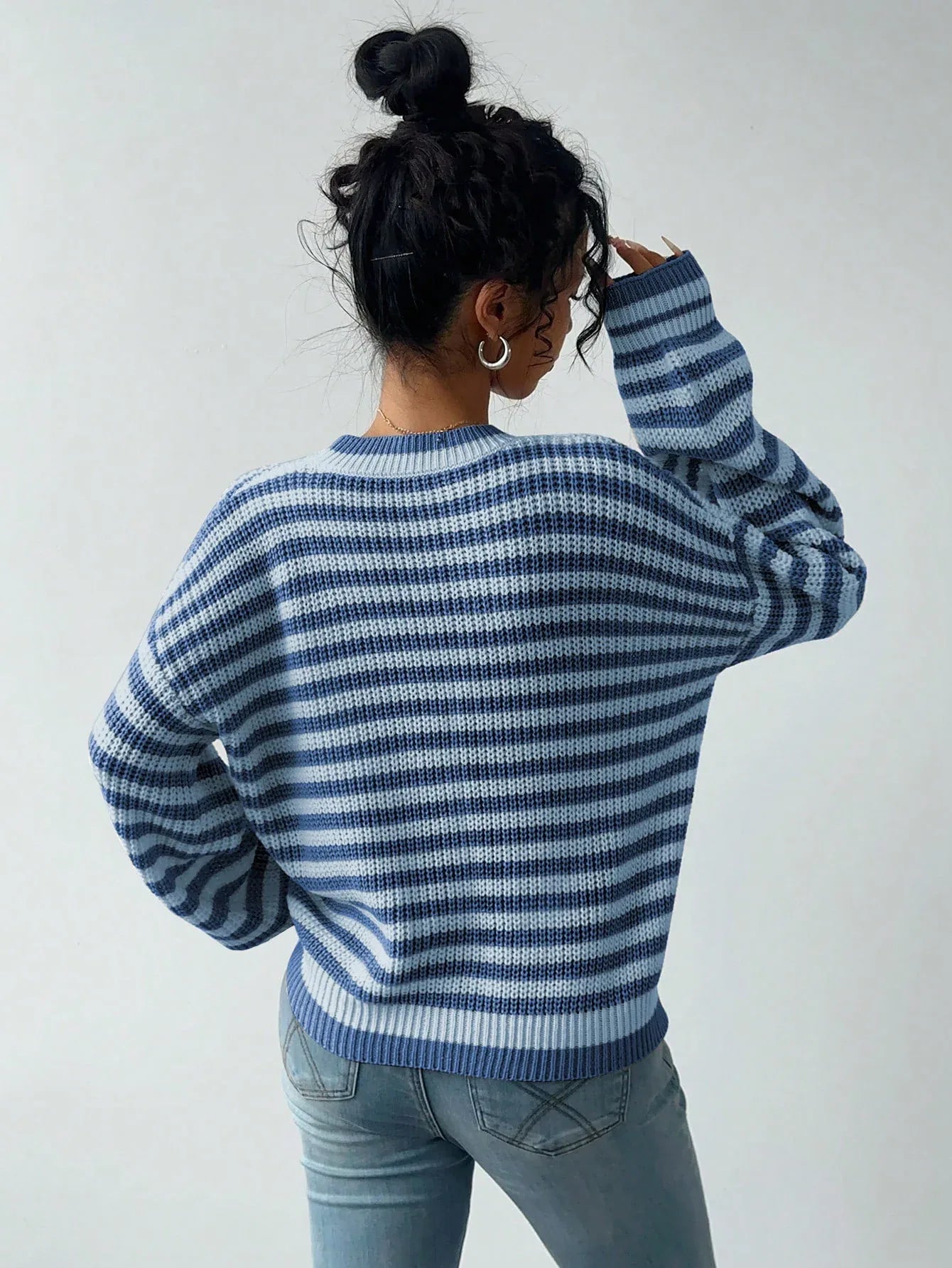 Rear view of a woman wearing a blue and white striped knit sweater with a crew neckline and long sleeves
