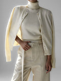 Woman wearing a cream-colored fine knit cardigan over a cream turtleneck and cream trousers