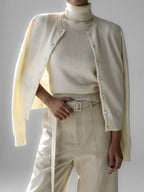 Woman wearing a cream-colored fine knit cardigan over a cream turtleneck and cream trousers